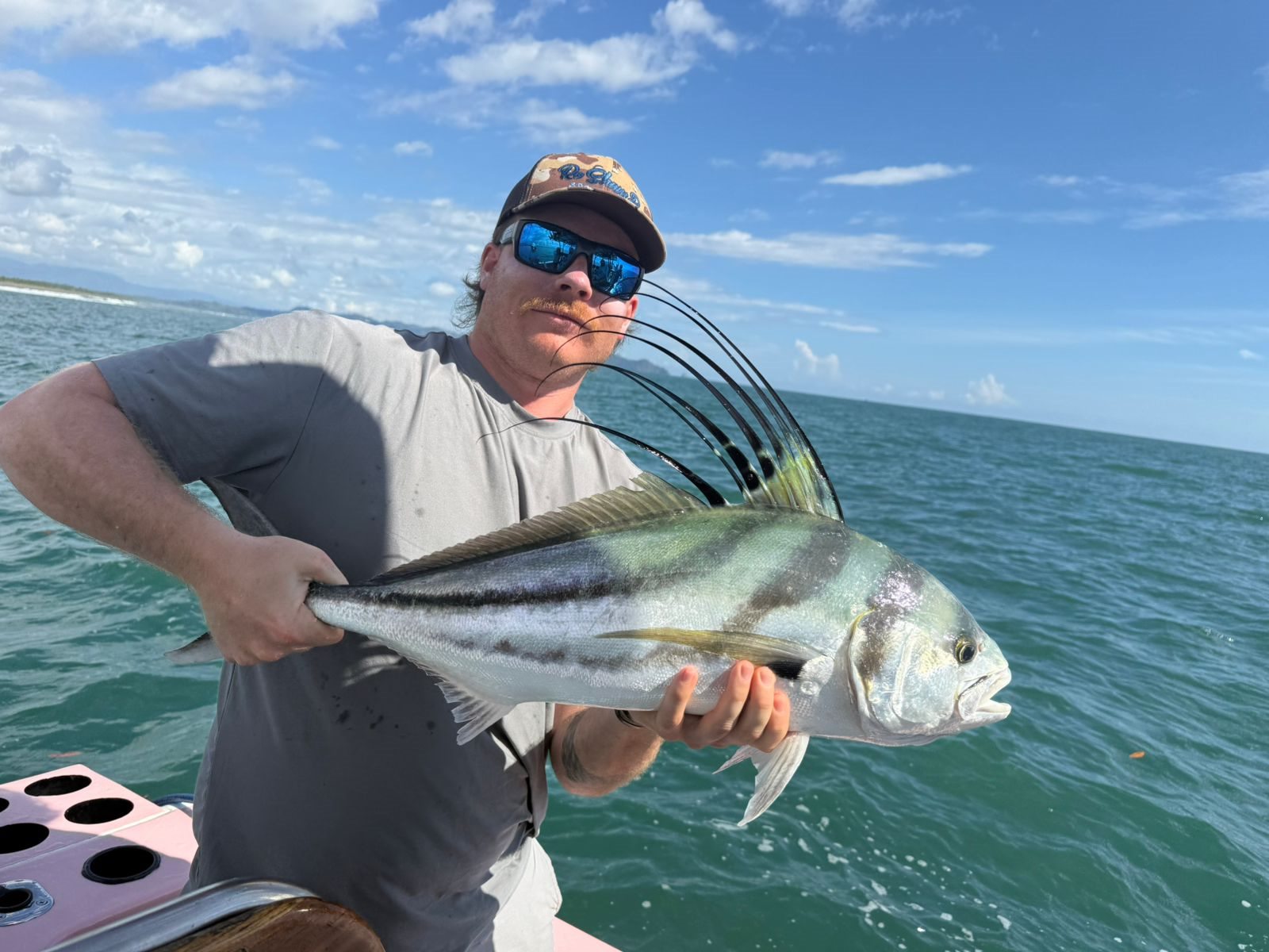 Angler displaying a roosterfish beside the pink charter boat