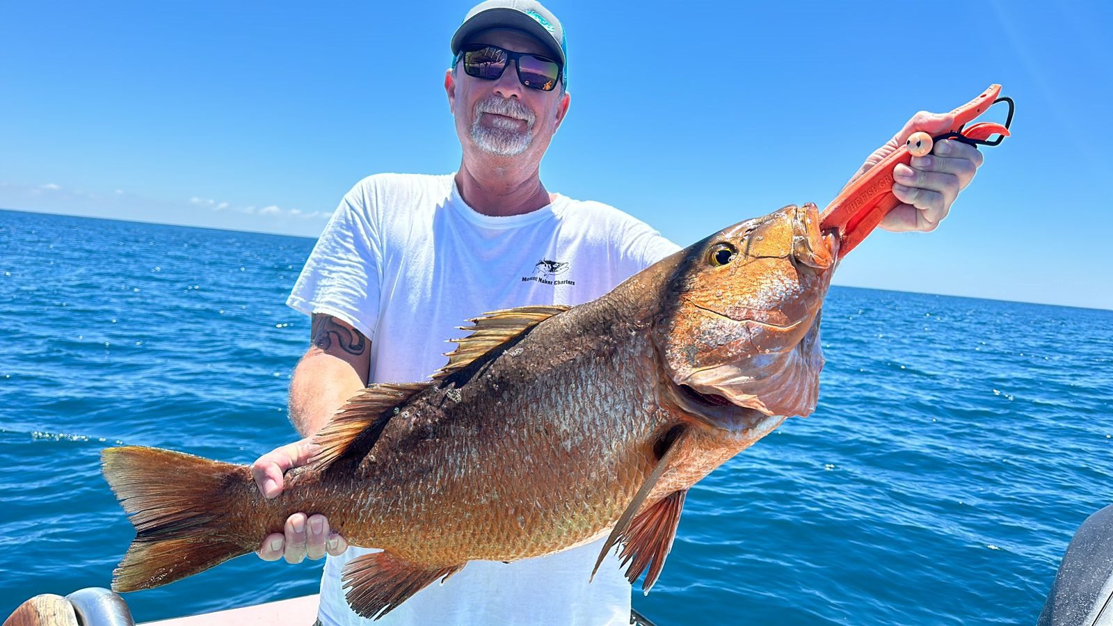 Angler presenting a large snapper against blue Pacific water